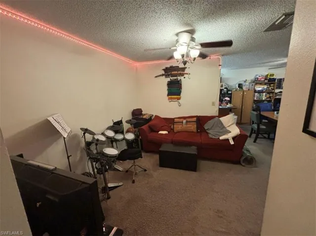 Living room with a textured ceiling, ceiling fan, and carpet floors