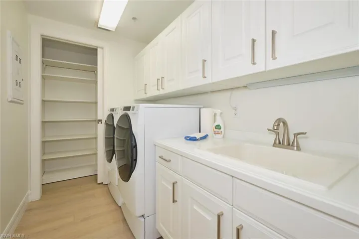 Laundry room with light wood-style floors, baseboards, washing machine and clothes dryer, a sink, and cabinet space