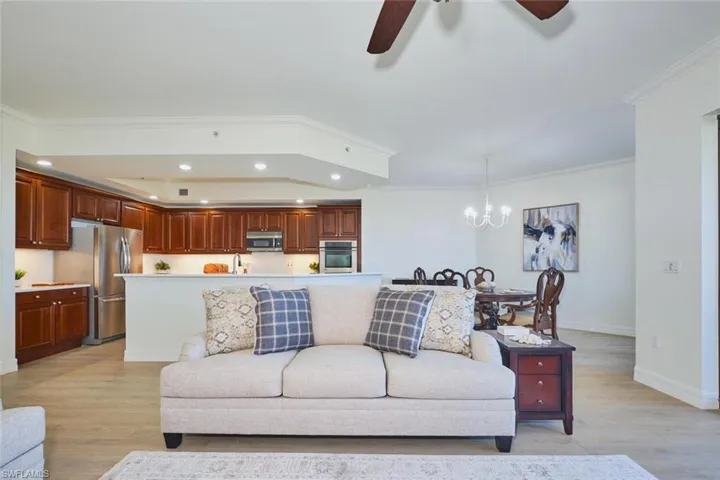 Living area with light wood-type flooring, recessed lighting, ceiling fan with notable chandelier, and crown molding