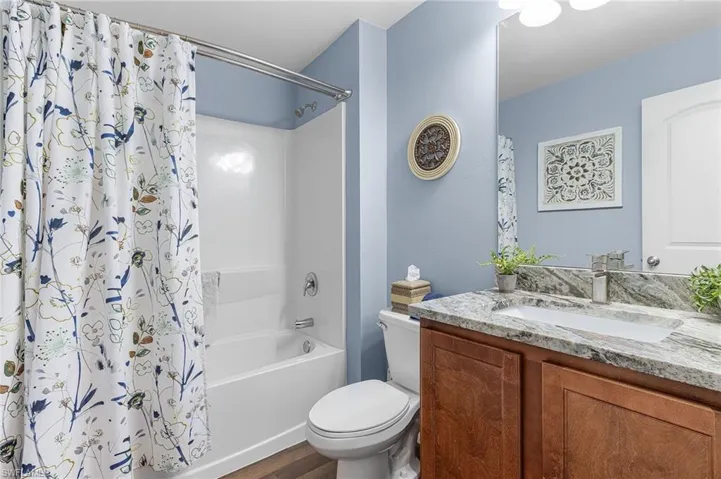 Full bathroom featuring shower / bath combo with shower curtain, vanity, and dark wood-style floors