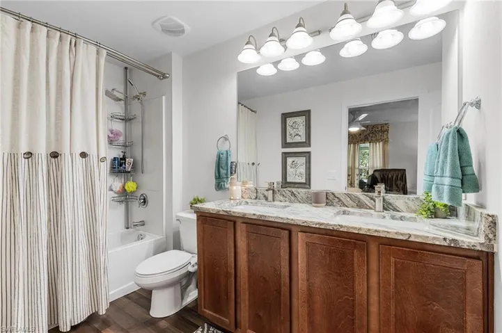 Full bathroom featuring shower / bath combination with curtain, dark wood finished floors, and double vanity