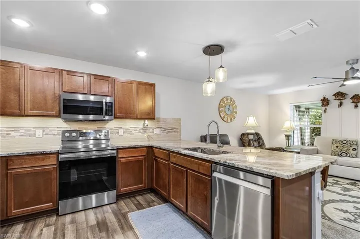 Kitchen with appliances with stainless steel finishes, open floor plan, a peninsula, light stone counters, and hanging light fixtures