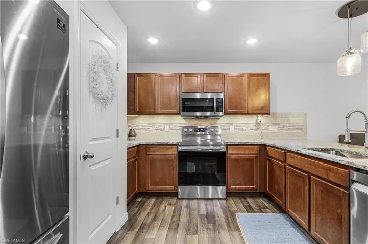 Kitchen with stainless steel appliances, decorative backsplash, light stone counters, brown cabinets, and recessed lighting