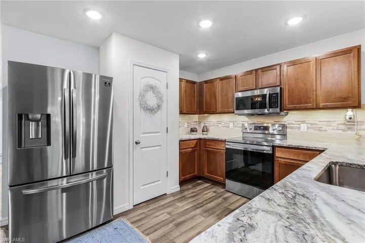 Kitchen featuring stainless steel appliances, decorative backsplash, light stone countertops, brown cabinetry, and light wood-type flooring