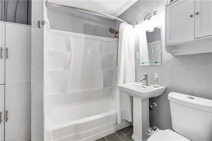 Bathroom featuring a white shower-tub combination, pedestal sink with chrome faucet, toilet, and white built-in cabinetry