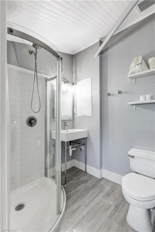 Contemporary bathroom featuring a curved glass shower enclosure with subway tile surround, a modern pedestal sink, and plank-style tile flooring