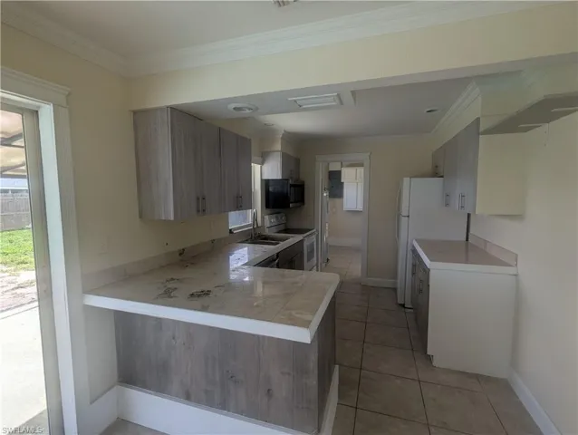 Kitchen with light countertops, ornamental molding, white appliances, light tile patterned flooring, and a peninsula