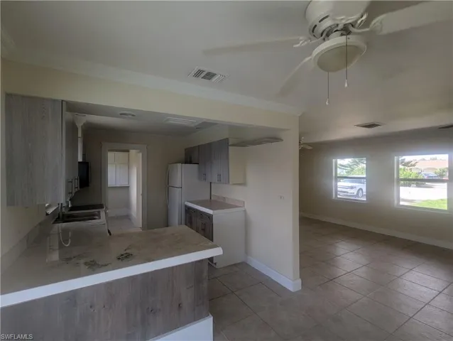 Kitchen with ceiling fan, ornamental molding, light tile patterned floors, light countertops, and freestanding refrigerator