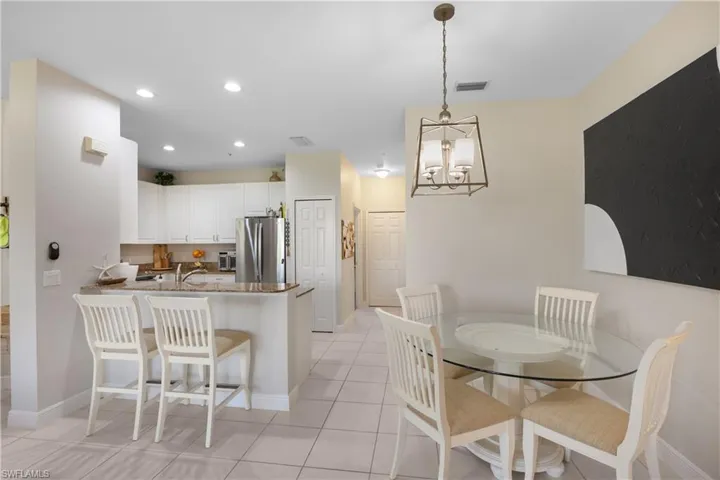 Kitchen featuring kitchen peninsula, light tile patterned floors, decorative light fixtures, white cabinetry, and stainless steel refrigerator