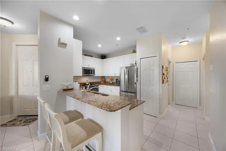 Kitchen featuring stone counters, sink, kitchen peninsula, white cabinets, and appliances with stainless steel finishes