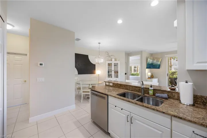 Kitchen with light stone counters, sink, white cabinets, and stainless steel dishwasher