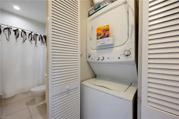 Clothes washing area featuring light tile patterned floors and stacked washer and clothes dryer