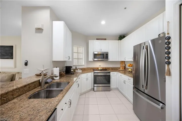 Kitchen with white cabinetry, sink, stainless steel appliances, dark stone counters, and light tile patterned flooring