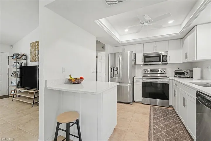 Kitchen with stainless steel appliances, white cabinets, light stone counters, a kitchen breakfast bar, and a ceiling fan