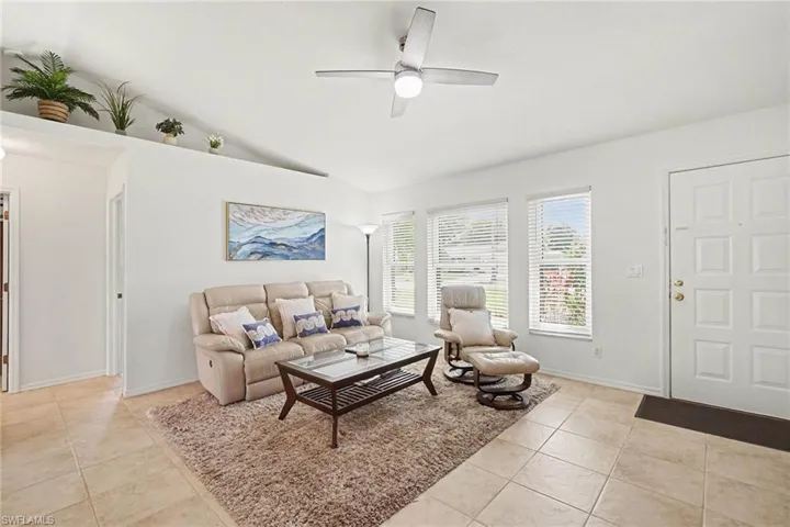 Living room featuring a ceiling fan, light tile patterned flooring, and vaulted ceiling