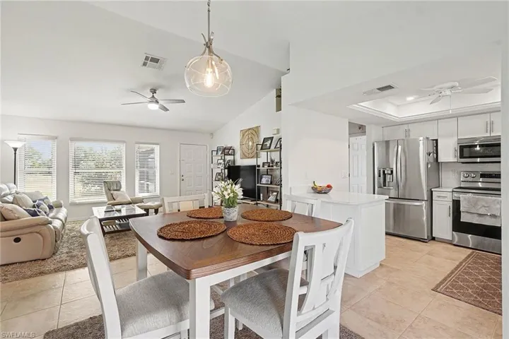 Dining space with a ceiling fan, light tile patterned floors, a tray ceiling, and vaulted ceiling