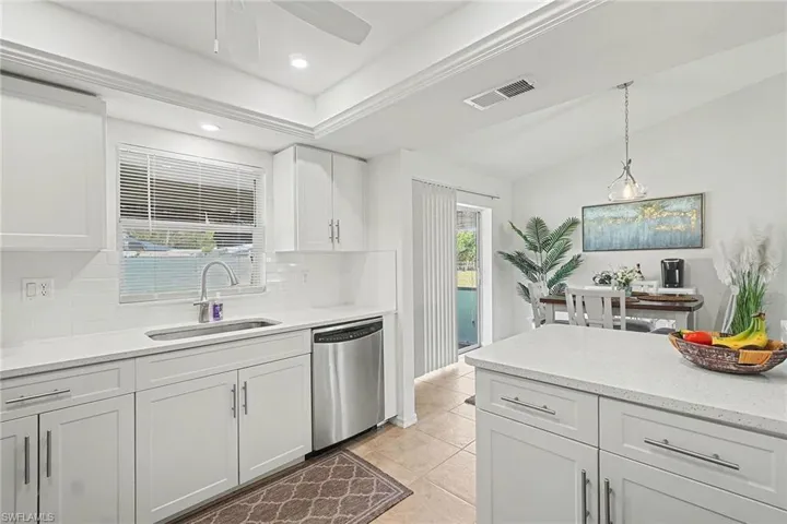 Kitchen with white cabinetry, stainless steel dishwasher, plenty of natural light, light stone counters, and vaulted ceiling