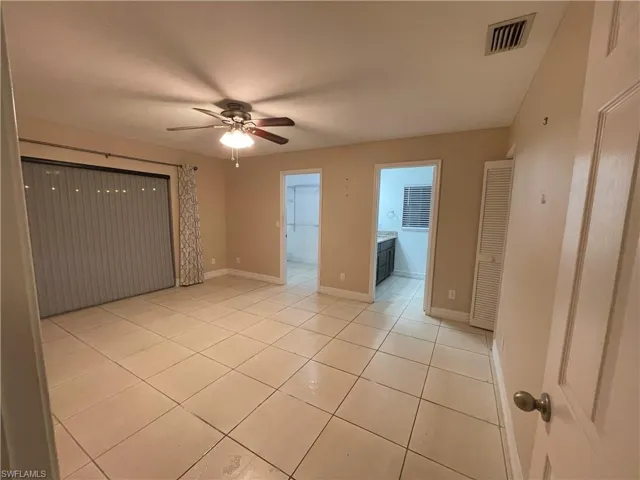 Unfurnished bedroom with light tile patterned floors, a spacious closet, ensuite bathroom, and ceiling fan