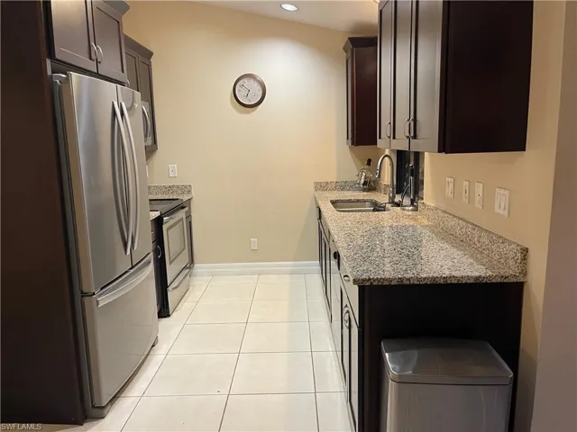 Kitchen with light stone counters, stainless steel appliances, light tile patterned floors, dark brown cabinets, and recessed lighting
