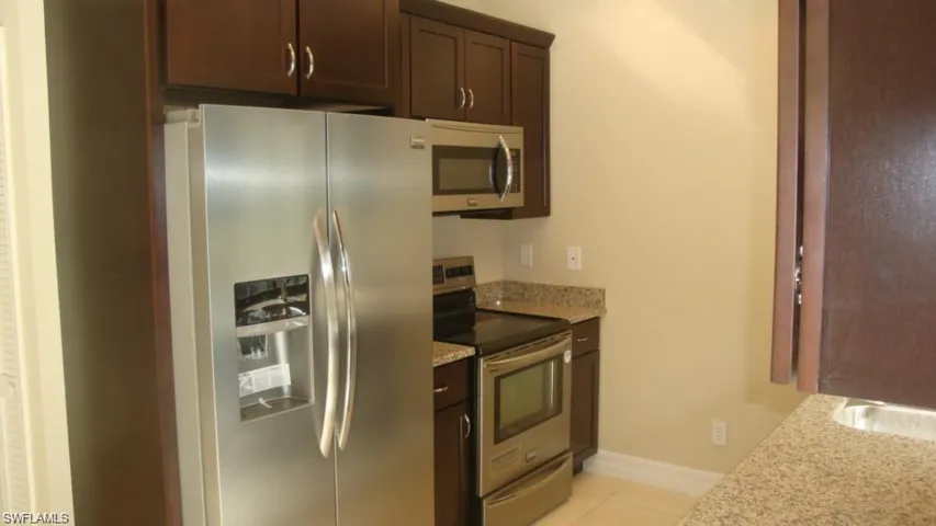 Kitchen with appliances with stainless steel finishes, light stone counters, dark brown cabinets, and light tile patterned floors