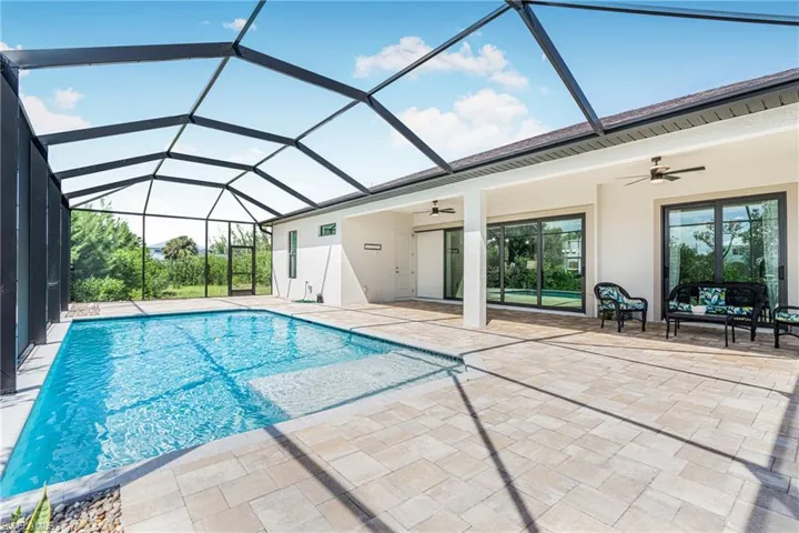 View of swimming pool featuring glass enclosure, ceiling fan, and a patio area