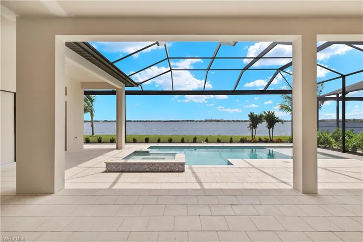 View of pool featuring a patio area, glass enclosure, a water view, and an in ground hot tub