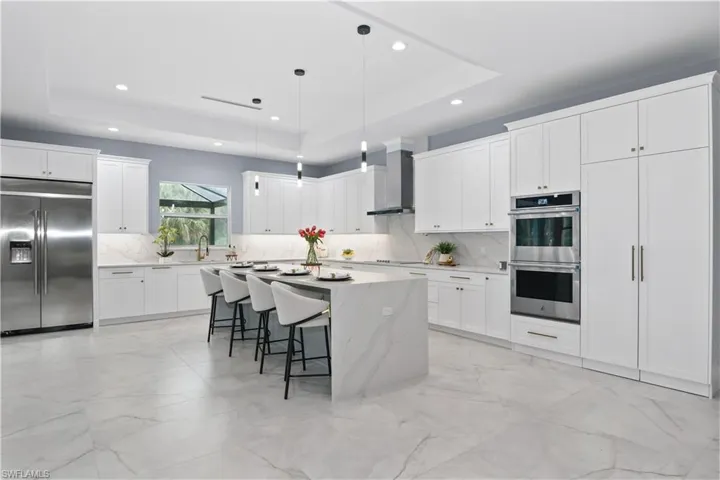 Kitchen featuring stainless steel appliances, a raised ceiling, wall chimney exhaust hood, and a kitchen island