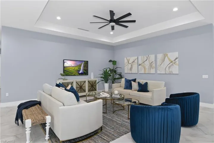 Living room featuring light tile patterned flooring, ceiling fan, and a raised ceiling