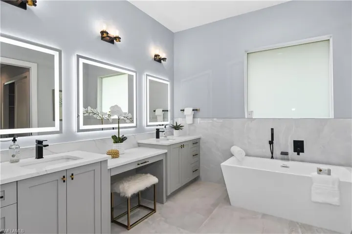 Bathroom with dual vanity, tile patterned flooring, tile walls, and a tub