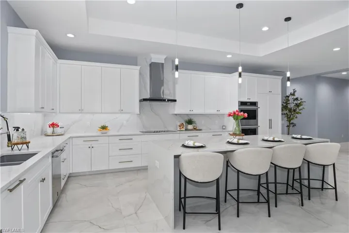 Kitchen featuring hanging light fixtures, stainless steel appliances, a raised ceiling, and wall chimney exhaust hood