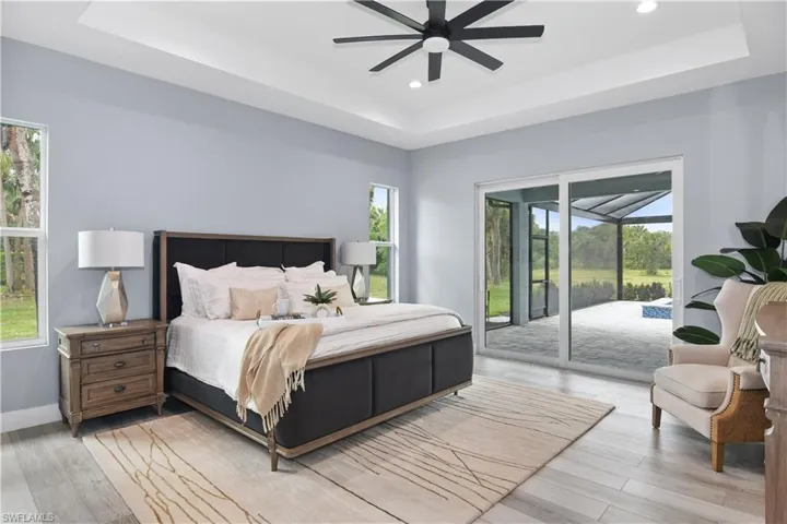 Bedroom featuring a raised ceiling, multiple windows, ceiling fan, and access to exterior