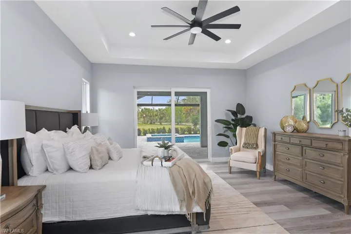 Bedroom featuring light hardwood / wood-style floors, a raised ceiling, access to outside, and ceiling fan