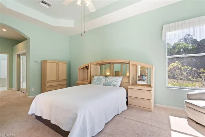 Bedroom featuring a tray ceiling, arched walkways, carpet, and a ceiling fan