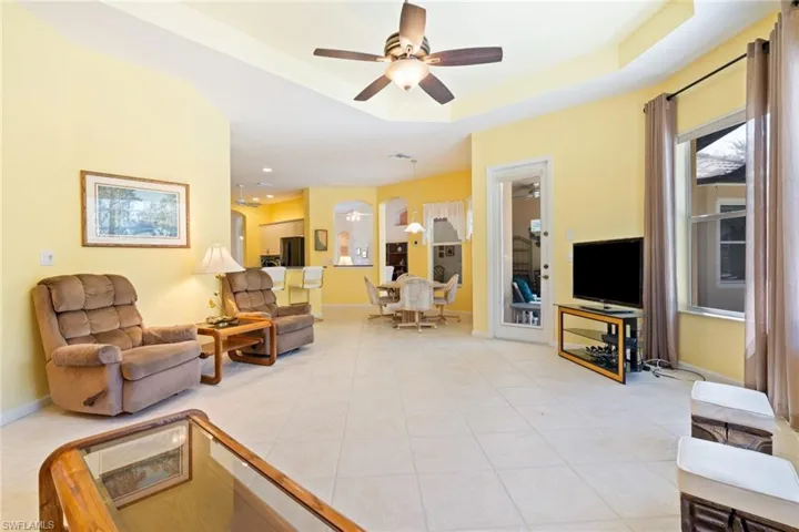 Living room featuring a ceiling fan, light tile patterned floors, a raised ceiling, and arched walkways