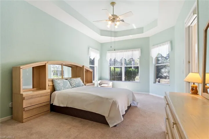 Bedroom featuring a ceiling fan, light colored carpet, and a tray ceiling