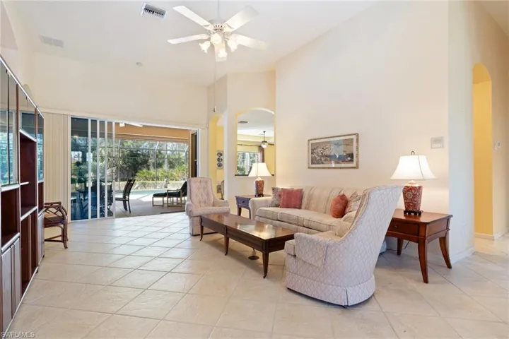 Living area with ceiling fan, arched walkways, a high ceiling, a sunroom, and light tile patterned floors