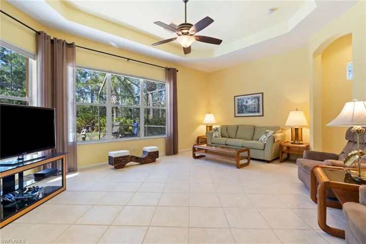 Living area featuring ceiling fan, a tray ceiling, light tile patterned floors, and arched walkways