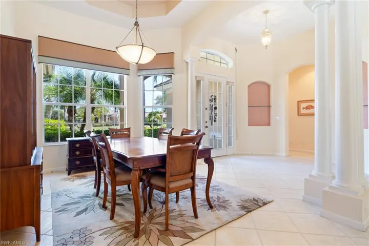 Dining room featuring decorative columns, arched walkways, light tile patterned flooring, and a tray ceiling