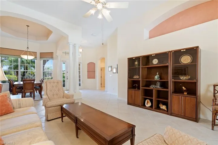 Living room with arched walkways, a ceiling fan, a tray ceiling, light tile patterned flooring, and ornate columns