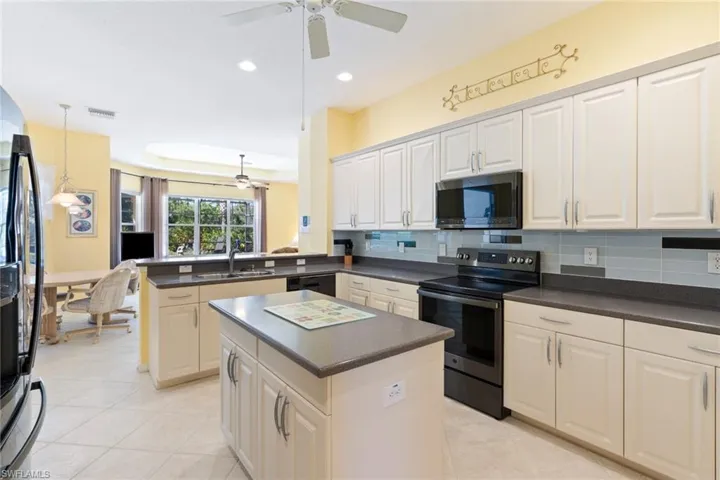 Kitchen featuring stainless steel appliances, dark countertops, a peninsula, a ceiling fan, and a center island