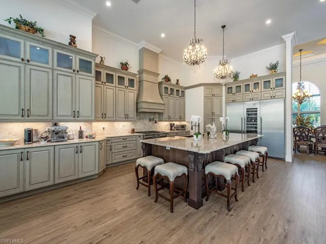 Kitchen featuring light stone countertops, a notable chandelier, wood-type flooring, a kitchen island with sink, and ornamental molding