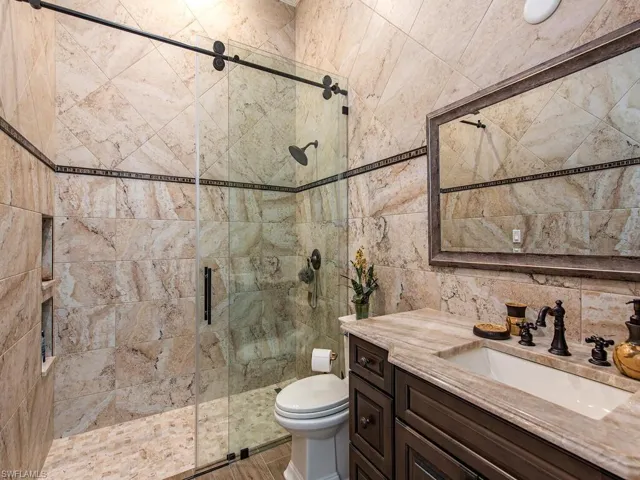 Bathroom with a shower with door, vanity, toilet, and tile walls