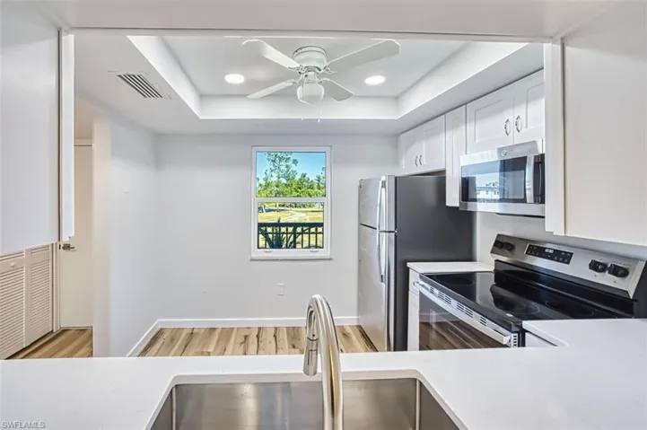 Kitchen featuring stainless steel appliances, white cabinets, recessed lighting, light wood-style flooring, and a tray ceiling