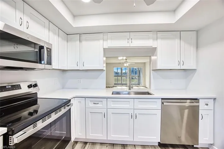 Kitchen with ceiling fan, stainless steel appliances, white cabinetry, and a raised ceiling