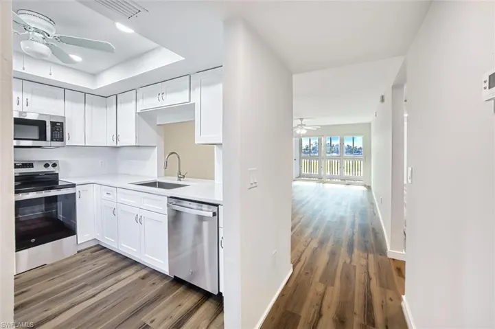 Kitchen featuring a ceiling fan, stainless steel appliances, white cabinets, and dark wood-type flooring