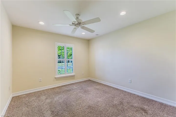 Carpeted room with a single window featuring white interior shutters