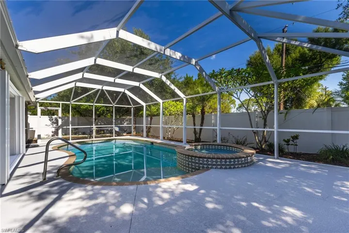 Screen-enclosed pool area featuring a curved swimming pool, an integrated spa with decorative tile, a light-colored paved deck, and a white privacy fence