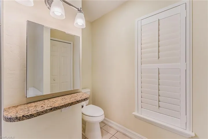 Bathroom featuring a floating vanity with a granite countertop, a wall-mounted mirror, and a three-light vanity fixture