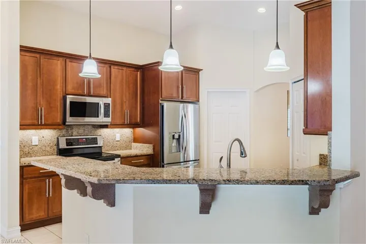 Kitchen featuring granite countertops, wood cabinetry, stainless steel appliances, pendant lighting, and an integrated sink with a high-arc faucet