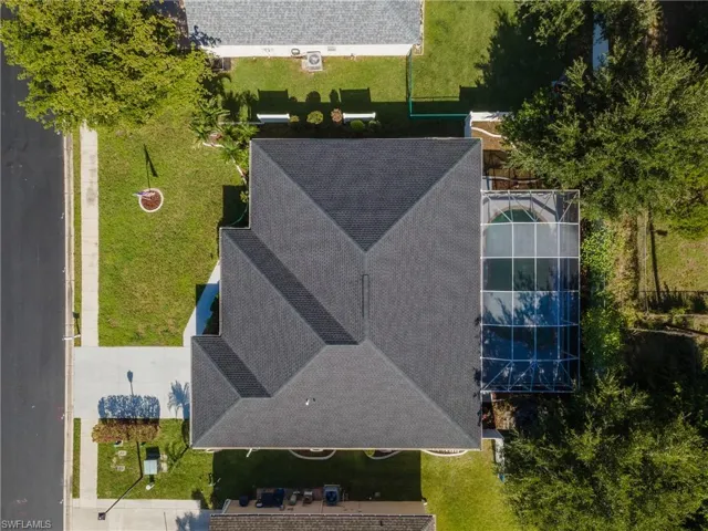 Aerial property perspective featuring a prominent multi-gabled roofline, screened pool enclosure, mature trees, and a concrete driveway